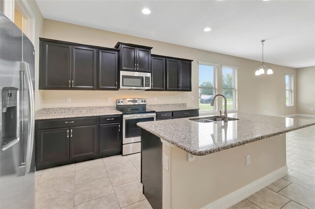 15531 Waterleigh Cove Dr, Winter Garden, FL 34787 - kitchen with stainless steel appliances, light stone counters, light tile patterned floors, dark cabinets, and an island with sink