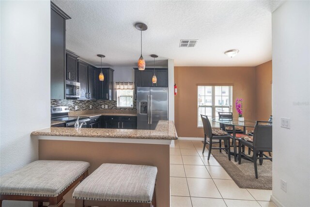212 Primrose Dr, Davenport, FL 33837 - kitchen with stainless steel appliances, a peninsula, pendant lighting, stone counters, and light tile patterned floors