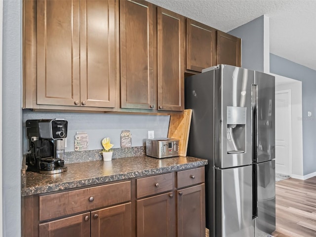1824 Forest Glen Dr, Fruitland Park, FL 34731 - kitchen with stainless steel refrigerator with ice dispenser, light wood-type flooring, baseboards, dark stone countertops, and a textured ceiling