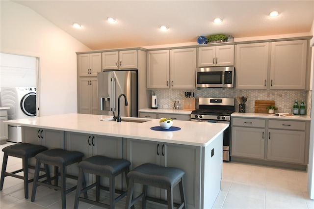 6301 Danielson Loop, The Villages, FL 32163 - kitchen with stainless steel appliances, washer / clothes dryer, decorative backsplash, gray cabinetry, and vaulted ceiling