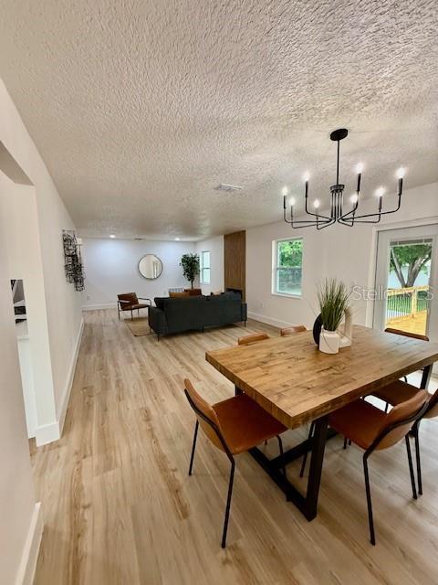 8203 Bluestar Cir, Orlando, FL 32819 - dining area with a textured ceiling, light wood-style floors, a chandelier, and baseboards