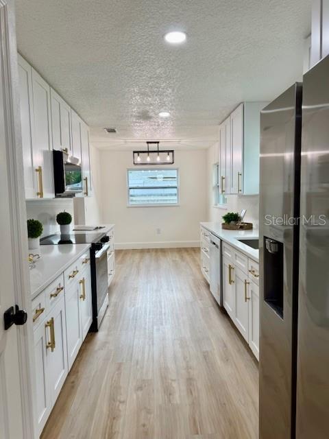 8203 Bluestar Cir, Orlando, FL 32819 - kitchen with stainless steel appliances, light wood-style floors, light countertops, a textured ceiling, and white cabinetry