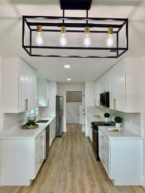 8203 Bluestar Cir, Orlando, FL 32819 - kitchen with appliances with stainless steel finishes, a sink, white cabinetry, light wood-style floors, and a textured ceiling