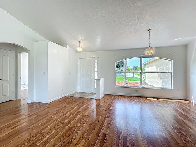 439 Gentle Breeze Dr, Minneola, FL 34715 - unfurnished living room with a chandelier, wood finished floors, baseboards, arched walkways, and a textured ceiling