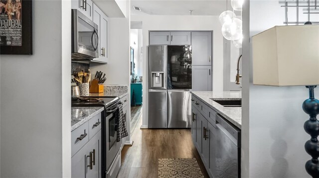 1130 Woodsong Way, Clermont, FL 34714 - kitchen featuring appliances with stainless steel finishes, gray cabinetry, dark wood-style flooring, light stone countertops, and decorative light fixtures