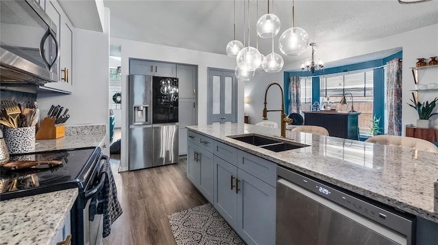 1130 Woodsong Way, Clermont, FL 34714 - kitchen featuring stainless steel appliances, a sink, light stone countertops, wood finished floors, and a chandelier