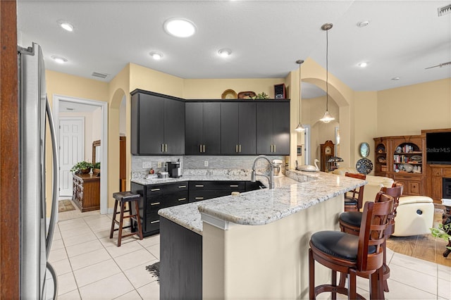 39145 Treeline Dr, Lady Lake, FL 32159 - kitchen featuring dark cabinetry, freestanding refrigerator, arched walkways, a kitchen breakfast bar, and a peninsula