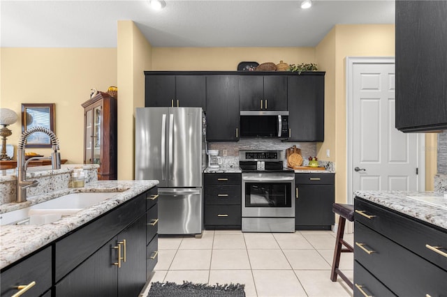 39145 Treeline Dr, Lady Lake, FL 32159 - kitchen featuring stainless steel appliances, a sink, dark cabinetry, light tile patterned floors, and backsplash