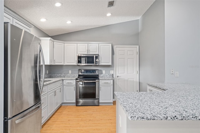 2557 Privada Dr, The Villages, FL 32162 - kitchen featuring stainless steel appliances, vaulted ceiling, a textured ceiling, light wood-type flooring, and white cabinetry
