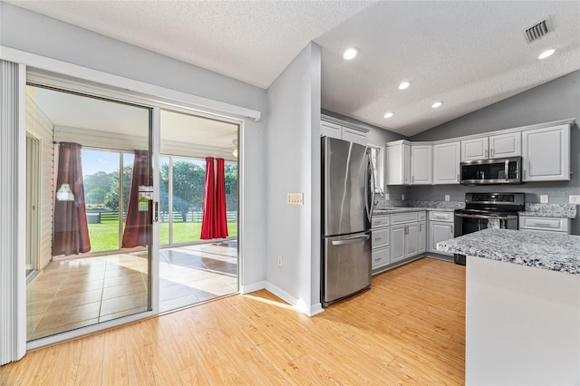 2557 Privada Dr, The Villages, FL 32162 - kitchen featuring stainless steel appliances, light wood-type flooring, a textured ceiling, vaulted ceiling, and light stone countertops