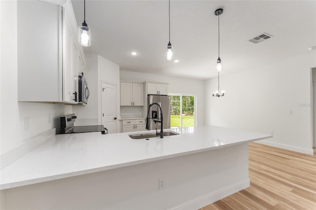 1809 W Linden Dr, Citrus Springs, FL 34434 - kitchen featuring appliances with stainless steel finishes, a peninsula, white cabinets, light wood-style floors, and hanging light fixtures