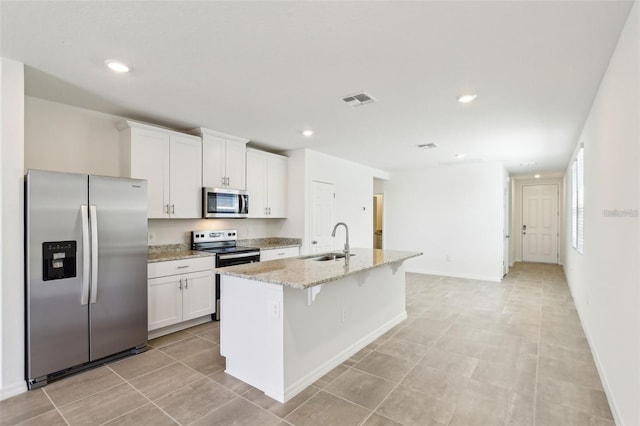 4973 Kaia Ave, Winter Haven, FL 33884 - kitchen with appliances with stainless steel finishes, a sink, white cabinetry, an island with sink, and light stone countertops