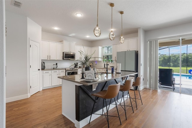 637 Neptune Dr, Groveland, FL 34736 - kitchen featuring appliances with stainless steel finishes, light wood finished floors, a kitchen bar, white cabinetry, and recessed lighting