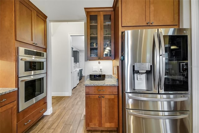 6008 Apex Way, Lady Lake, FL 32159 - kitchen with appliances with stainless steel finishes, light wood-style floors, light stone counters, glass insert cabinets, and brown cabinets