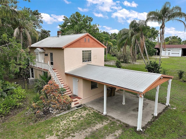 27113 Robertson Rd, Yalaha, FL 34797 - back of property featuring stucco siding, an attached carport, dirt driveway, stairway, and metal roof