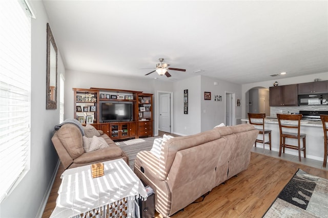 9785 Pepper Tree Trl, Wildwood, FL 34785 - living area featuring arched walkways, ceiling fan, light wood finished floors, and plenty of natural light