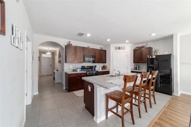 9785 Pepper Tree Trl, Wildwood, FL 34785 - kitchen with black appliances, arched walkways, a textured ceiling, light countertops, and backsplash