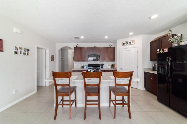 9785 Pepper Tree Trl, Wildwood, FL 34785 - kitchen featuring black appliances, arched walkways, a breakfast bar, tasteful backsplash, and a textured ceiling