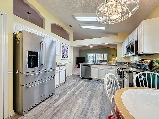 3716 Eversholt St, Clermont, FL 34711 - kitchen with appliances with stainless steel finishes, vaulted ceiling, a peninsula, light wood finished floors, and white cabinets