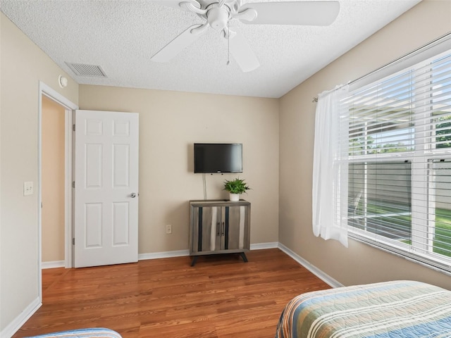 2369 Five Forks Trl, The Villages, FL 32162 - bedroom with multiple windows, wood finished floors, a textured ceiling, and a ceiling fan