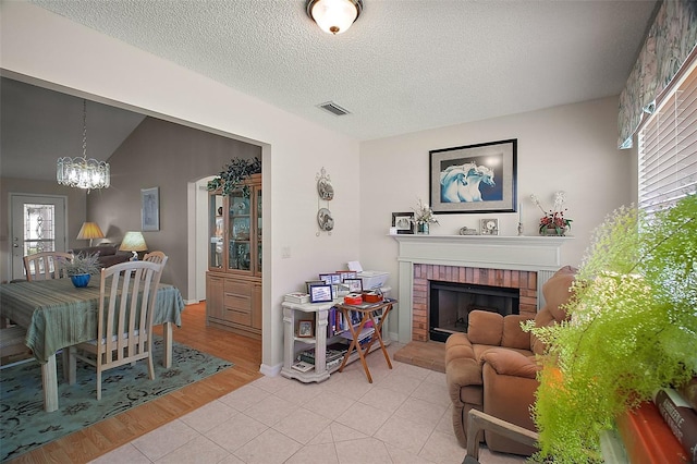 1007 Diego Ct, The Villages, FL 32159 - living room with a chandelier, a brick fireplace, a textured ceiling, and light wood-type flooring