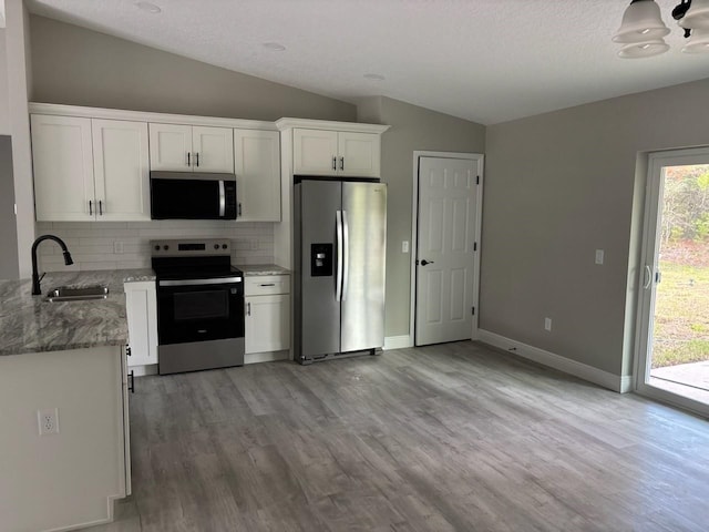 6769 N Waterman Dr, Dunnellon, FL 34433 - kitchen with appliances with stainless steel finishes, vaulted ceiling, light wood-style flooring, backsplash, and white cabinetry