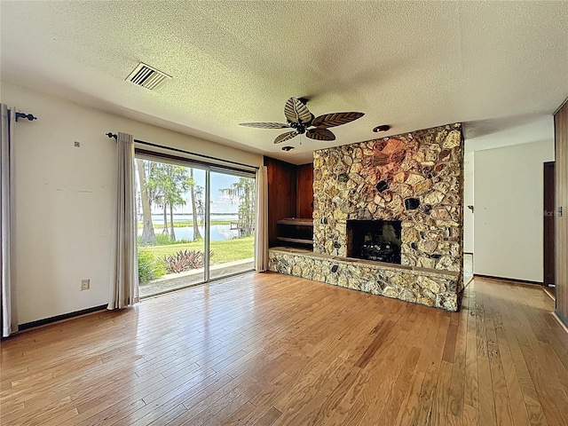 11401 Cypress Dr, Clermont, FL 34711 - unfurnished living room with a textured ceiling, light wood-style flooring, ceiling fan, a stone fireplace, and a water view
