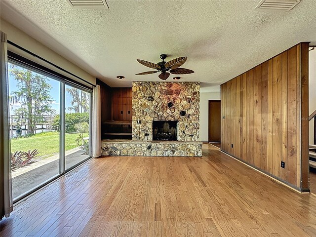 11401 Cypress Dr, Clermont, FL 34711 - unfurnished living room featuring a textured ceiling, wooden walls, light wood finished floors, a ceiling fan, and a stone fireplace