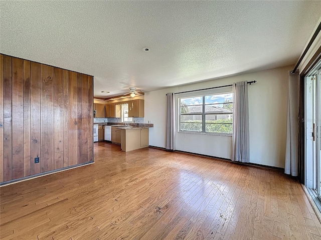 11401 Cypress Dr, Clermont, FL 34711 - kitchen featuring light wood finished floors, a textured ceiling, wood walls, open floor plan, and brown cabinets