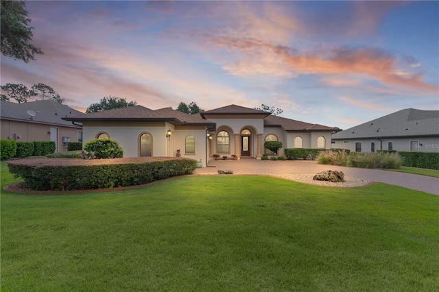 mediterranean / spanish house with curved driveway, a yard, and stucco siding
