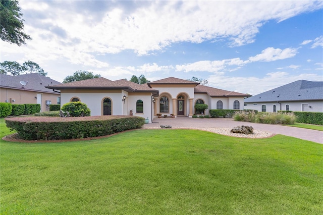 mediterranean / spanish-style home featuring stucco siding, a front yard, and curved driveway