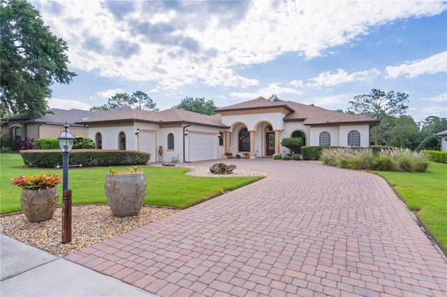 mediterranean / spanish-style house featuring curved driveway, a front lawn, an attached garage, and stucco siding
