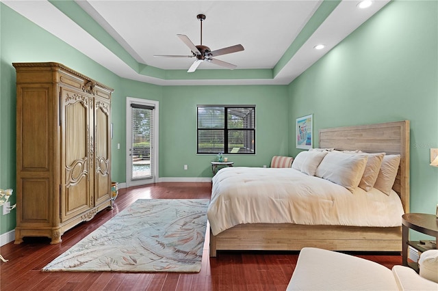 bedroom with access to exterior, a raised ceiling, recessed lighting, dark wood-style flooring, and a ceiling fan