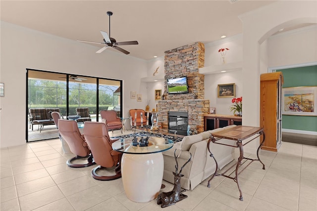 living room featuring ceiling fan, crown molding, a stone fireplace, light tile patterned floors, and a towering ceiling