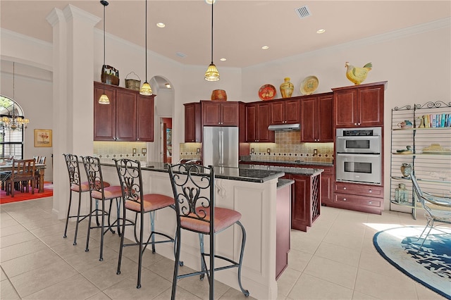 kitchen with appliances with stainless steel finishes, ornamental molding, a breakfast bar, decorative backsplash, and light tile patterned flooring