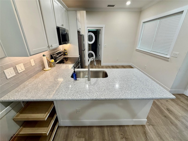 3607 Umbrella Tree Ln, Oxford, FL 34484 - kitchen featuring appliances with stainless steel finishes, stacked washing machine and dryer, light stone counters, and decorative backsplash