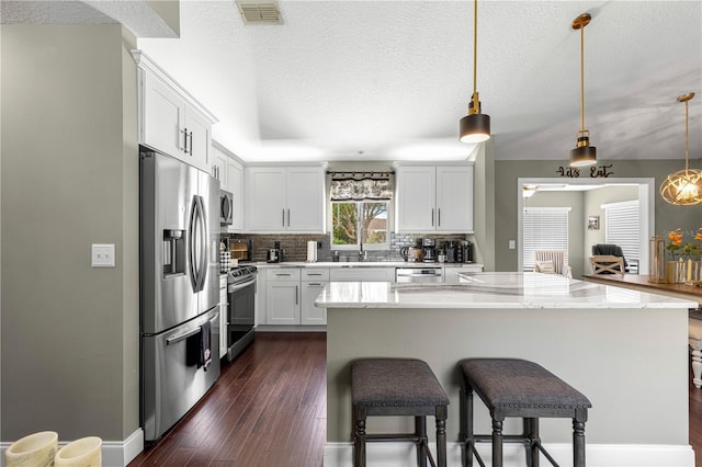 9790 SE 175th St, Summerfield, FL 34491 - kitchen featuring stainless steel appliances, tasteful backsplash, dark wood-style floors, a kitchen bar, and white cabinetry