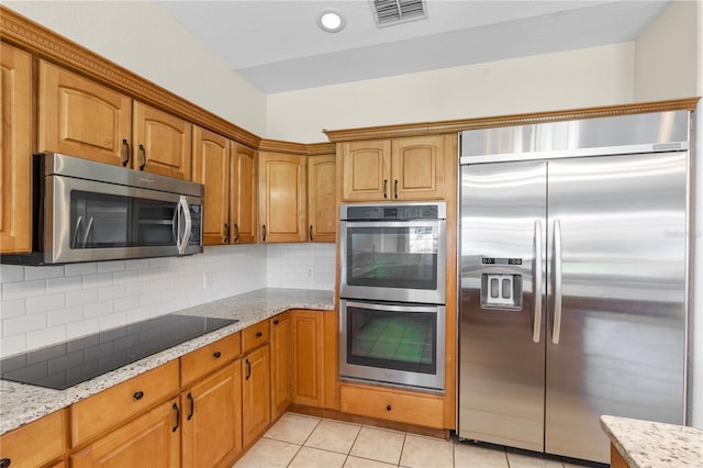81 N Carol Ave, Mascotte, FL 34753 - kitchen featuring appliances with stainless steel finishes, light stone countertops, decorative backsplash, light tile patterned floors, and brown cabinets