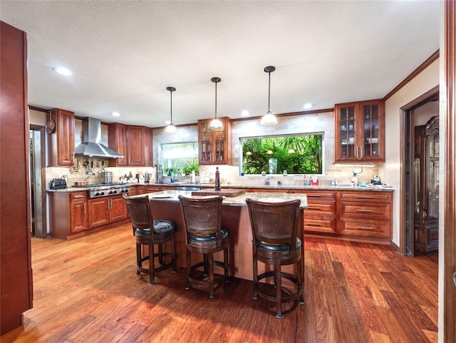 15733 Tower View Dr, Clermont, FL 34711 - kitchen featuring wall chimney range hood, stainless steel gas stovetop, wood finished floors, decorative backsplash, and a kitchen breakfast bar