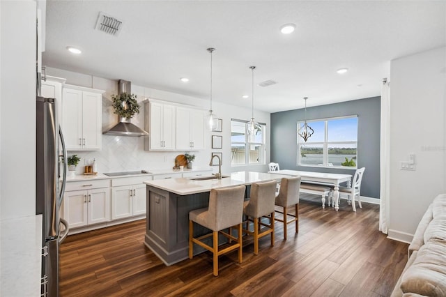 3304 Canna Lily Pl, Clermont, FL 34711 - kitchen with wall chimney range hood, freestanding refrigerator, dark wood finished floors, a breakfast bar area, and white cabinetry