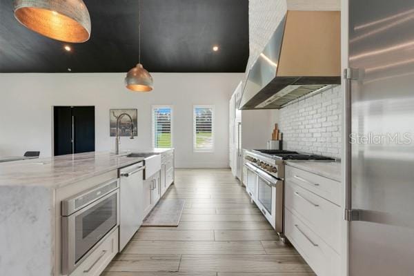 10711 County Road 561, Clermont, FL 34711 - kitchen featuring high end appliances, wall chimney exhaust hood, light wood-type flooring, white cabinets, and light stone countertops