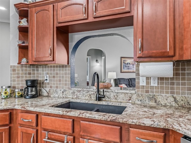 16863 SE 110th Court Rd, Summerfield, FL 34491 - kitchen featuring open shelves, backsplash, arched walkways, light stone counters, and brown cabinetry