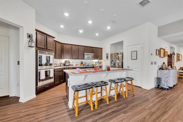 2488 Begonia St, Mascotte, FL 34753 - kitchen featuring appliances with stainless steel finishes, light wood-style floors, dark brown cabinets, a kitchen breakfast bar, and a kitchen island with sink
