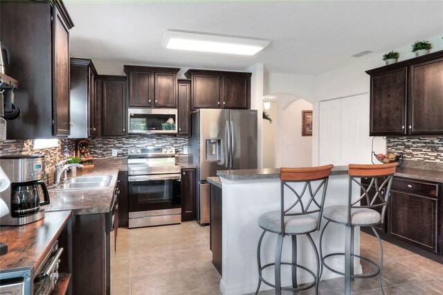 6906 Glenbrook Dr, Lakeland, FL 33811 - kitchen with stainless steel appliances, arched walkways, dark brown cabinetry, tasteful backsplash, and a kitchen island