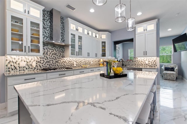 1702 Hidden Palms Dr, Davenport, FL 33897 - kitchen featuring wall chimney exhaust hood, stainless steel gas cooktop, a kitchen island, light marble finish floors, and backsplash
