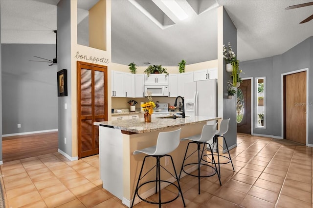 3184 Maltby Dr, Deltona, FL 32738 - kitchen featuring ceiling fan, white appliances, a kitchen breakfast bar, white cabinets, and light stone counters