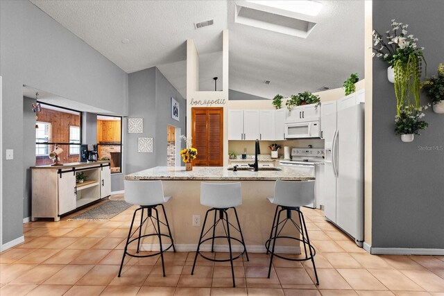3184 Maltby Dr, Deltona, FL 32738 - kitchen featuring white appliances, white cabinets, a center island with sink, light stone counters, and a breakfast bar