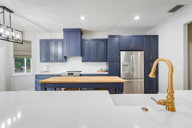 15629 Catherine Cir, Groveland, FL 34736 - kitchen with appliances with stainless steel finishes, custom exhaust hood, a chandelier, decorative backsplash, and blue cabinetry