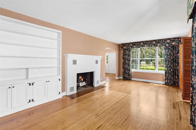 9223 Silver Lake Dr, Leesburg, FL 34788 - unfurnished living room featuring arched walkways, light wood-style flooring, a fireplace, and built in shelves