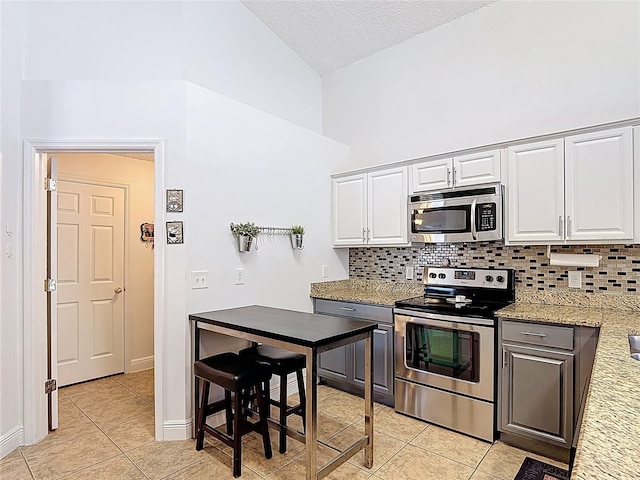 167 Castaway Beach Way, Kissimmee, FL 34746 - kitchen with stainless steel appliances, light tile patterned flooring, tasteful backsplash, white cabinetry, and high vaulted ceiling